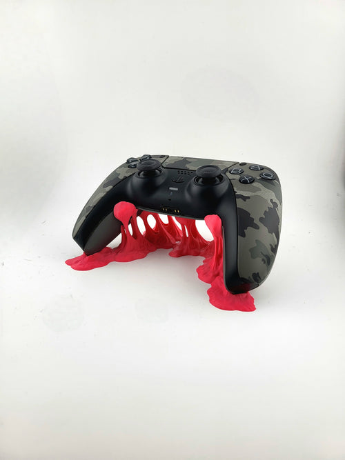 Front three-quarter view of a red 3D printed slime stand supporting a camouflage PS5 DualSense controller above rising tendrils.