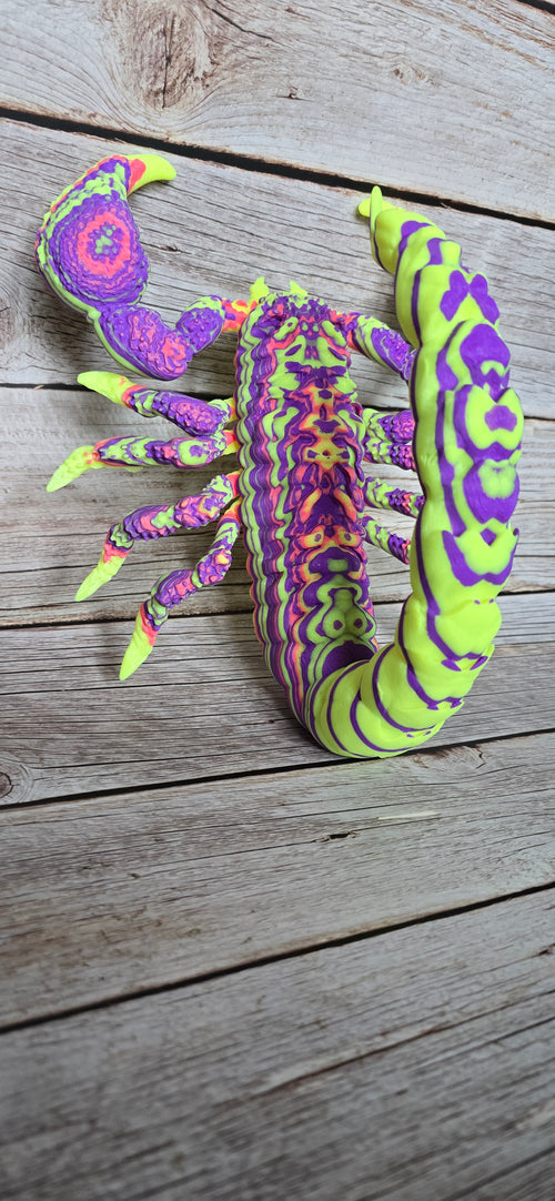 Psychedelic scorpion wall sculpture in neon green, purple, pink and orange with raised claws, pointed legs and a curled stinger.