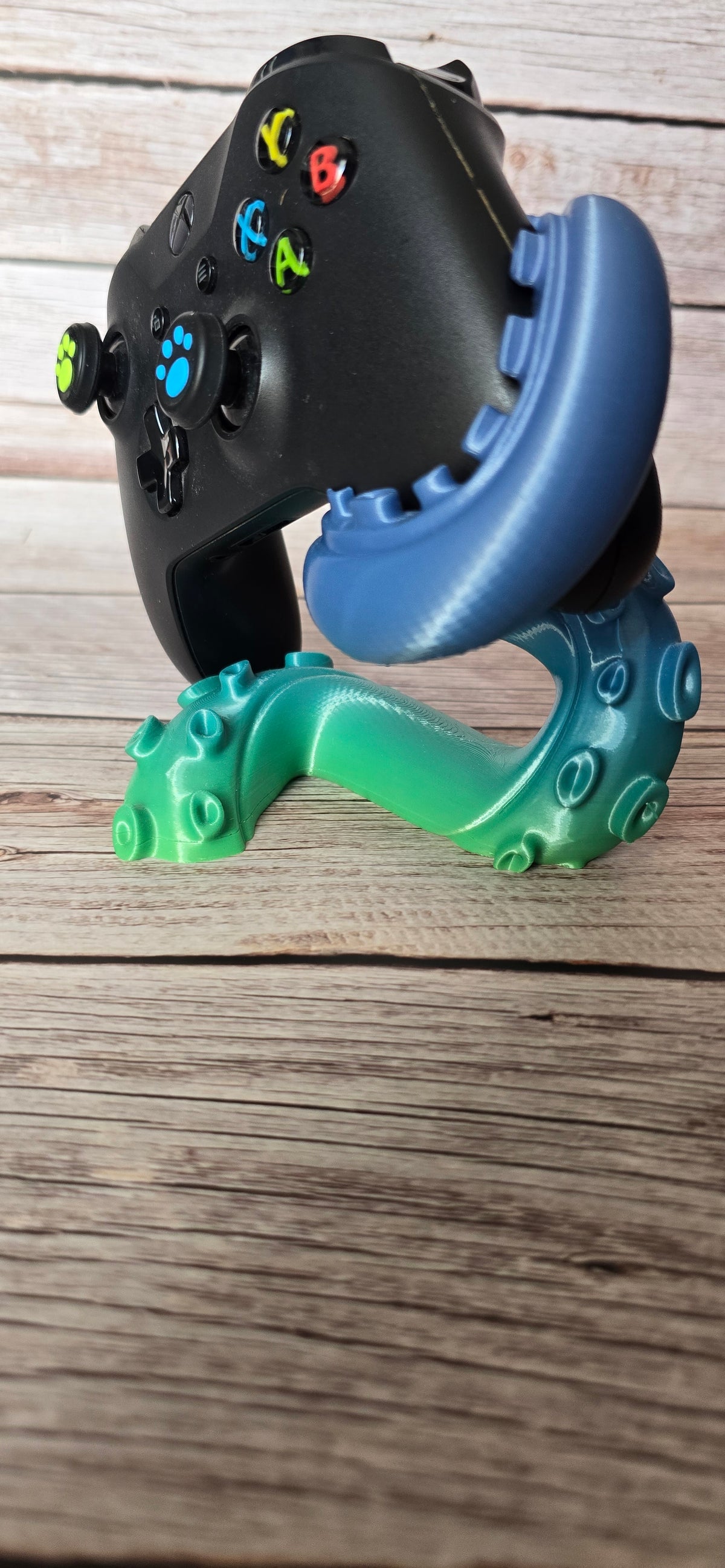 Side view of the Abyssal Reach Xbox controller holder showing its sweeping tentacle, raised sucker details and teal-blue finish.