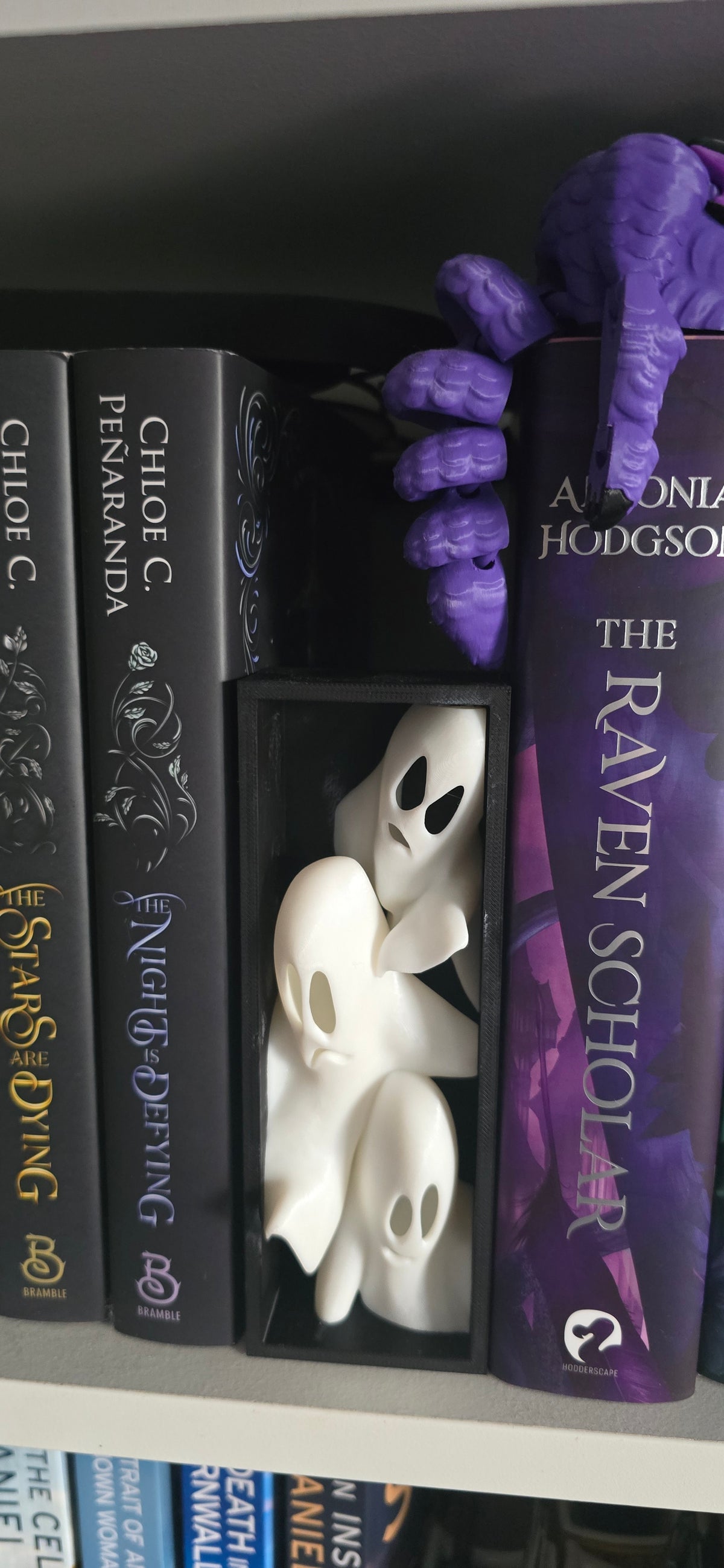 Close front view of the Whispering Shelf ghost book nook showing three smooth white spirits with dark eye and mouth openings.