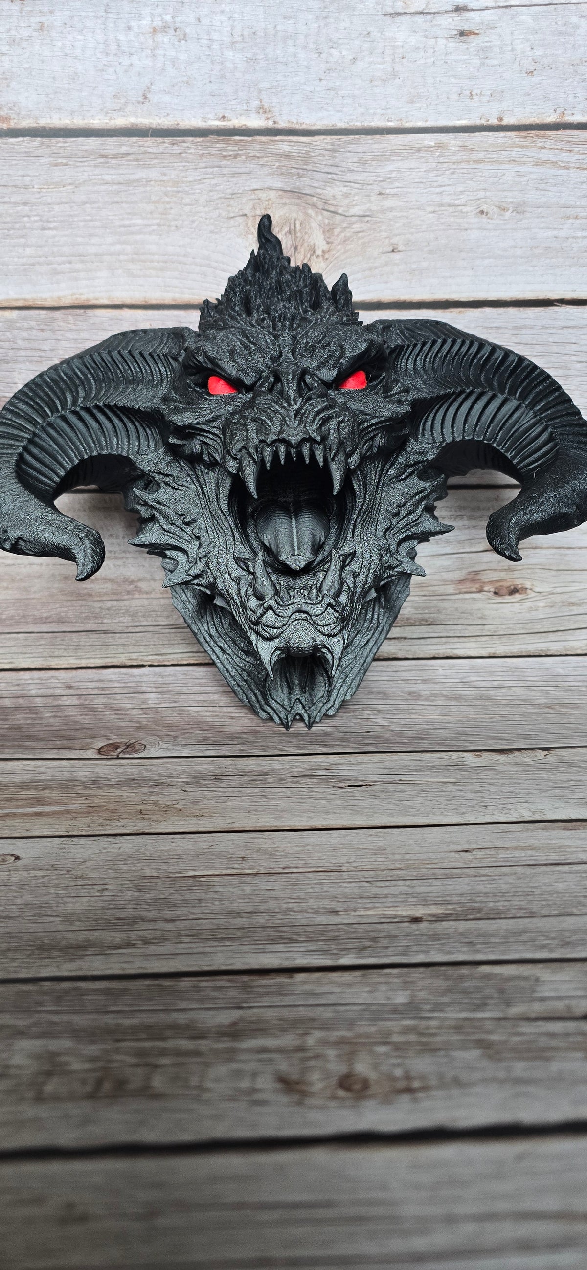 Front view of the Ashen Hornlord demon skull wall art showing its symmetrical horns, open mouth, long fangs and red eye details.