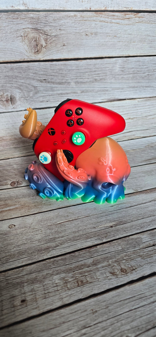 Front three-quarter view of a colourful Kraken controller stand holding a red Xbox-style controller between curled tentacles.