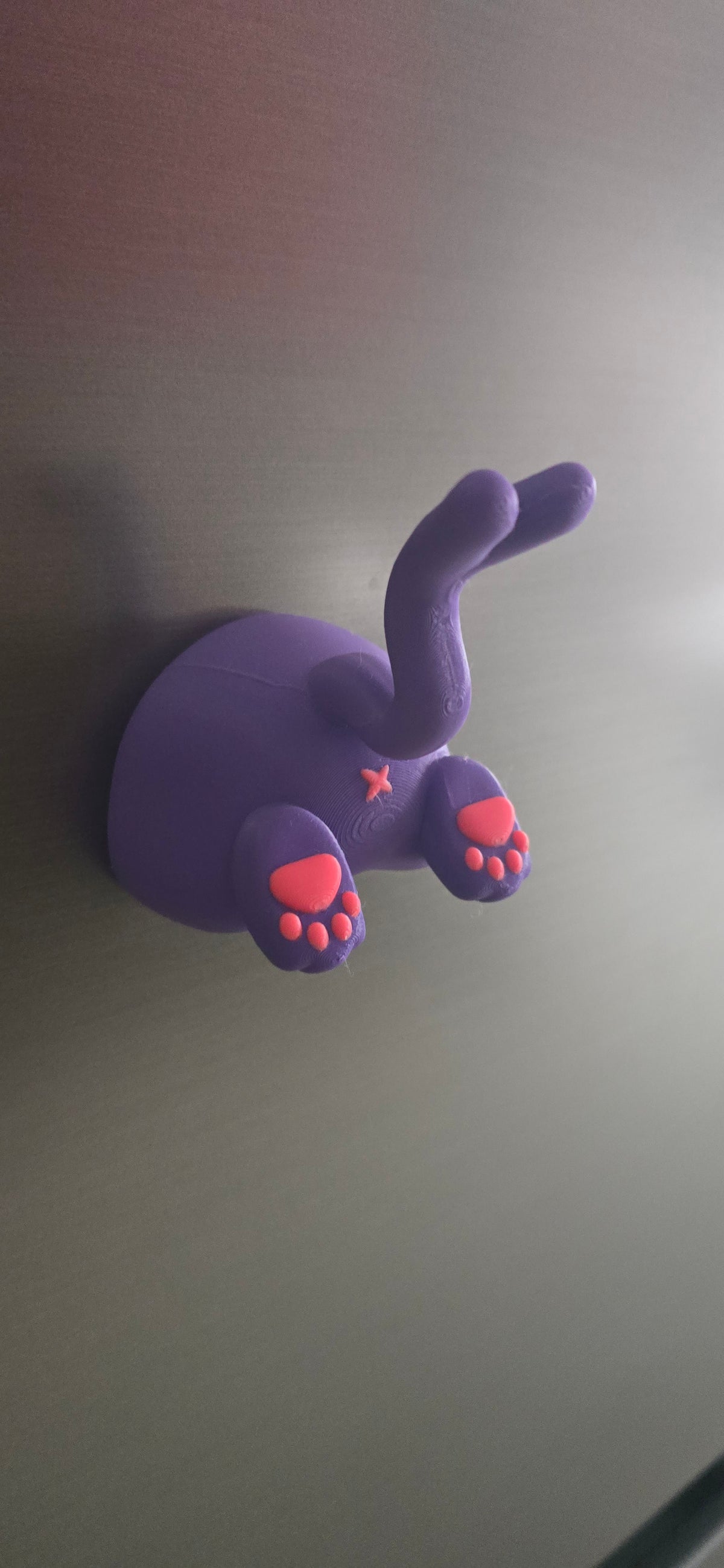 Front-angled view of the Dreamsplit Familiar fridge magnet with two raised paws, bright pink pads and a curved split-tip purple tail.