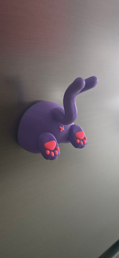 Front-angled view of the Dreamsplit Familiar fridge magnet with two raised paws, bright pink pads and a curved split-tip purple tail.